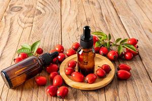 serum based on rosehip seed oil for facial skin care in a cosmetic bottles on a wooden background among ripe rosehip berries. moistening. nutrition. photo
