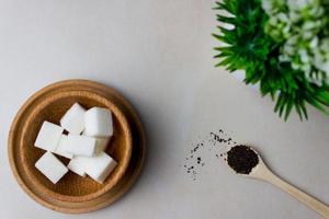 Sugar cubes in a wooden plate and spoon with tea feaves on the kitchen table with utensils and green plant. Making tea, tea break. Top view photo