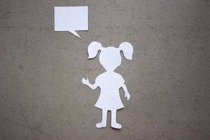 Silhouette of a girl in a dress and with ponytails made of white paper, cut by hand. In the center of the photo. On beige background photo