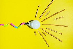 A creative composition of a light bulb and rays of light, a minimalistic concept, a tadpole, on a yellow background. photo