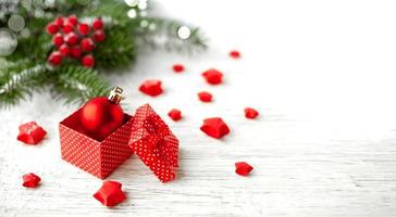 composición de vacaciones de año nuevo. rama de un árbol de navidad con frutos rojos, un regalo y baratijas en una tabla de madera clara. foto