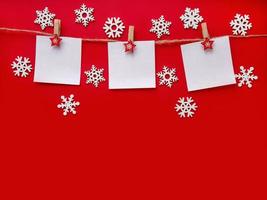 Christmas red background with white snowflakes. Three sheets of paper with space for text on a rope. Topview, copy space photo