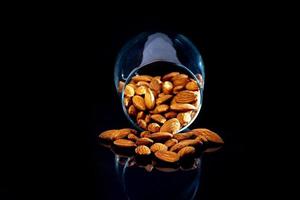 Peeled almond in jar wineglass bucket on a black isolated background. Row of bowls with almond nuts, front view. photo