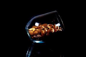 Peeled almond in jar wineglass bucket on a black isolated background. Row of bowls with almond nuts, front view. photo