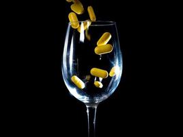 white orange pills in wineglass glass . in jar. in bucket Isolated on black set of capsule and pills inside closeup, photo