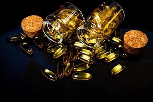 Fish oil capsules. Yellow omega 3 pills in jar on the dark black. fish oil capsules in wineglass glass . in jar. in bucket ampoules photo