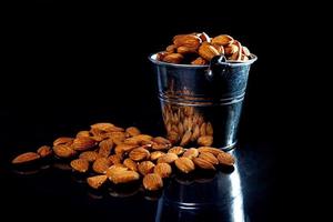 Peeled almond in jar wineglass bucket on a black isolated background. Row of bowls with almond nuts, front view. photo