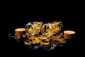 Fish oil capsules. Yellow omega 3 pills in jar on the dark black. fish oil capsules in wineglass glass . in jar. in bucket ampoules photo