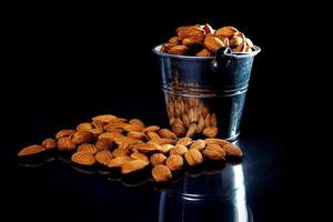 Peeled almond in jar wineglass bucket on a black isolated background. Row of bowls with almond nuts, front view. photo