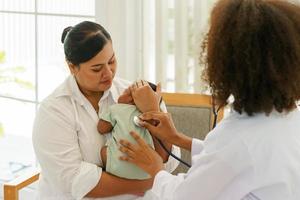 un bebé recién nacido de un mes de edad, de raza mixta africano-tailandés, visitando al médico para un chequeo de salud con estetoscopio en la clínica pediátrica. consulta de concepto, chequeo, enfermera, bebé curativo. foto