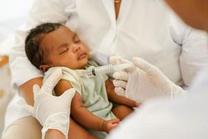 primer plano de la mano y la aguja. el médico sostiene una jeringa para vacunar a un bebé recién nacido de un mes con una inyección. concepto clínica pediatra control de salud vacuna antivirus para bebés. foto
