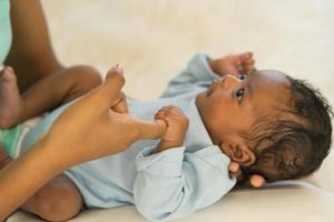 bebé recién nacido africano de un mes sosteniendo los dedos de la mano de la madre, sonríe y mira, relájate sin preocupaciones. imagen con poca profundidad de campo, seleccione el área de enfoque de la mano. foto