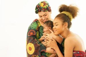 Mother and eldest daughter in traditional dress native-style African carry newborn baby one-month-old breastfeeding. Happy infant mixed race afro-Asia sleep well in warm embrace of motherhood. photo