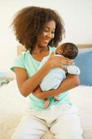 joven madre afroamericana sosteniendo a su hijo recién nacido de un mes con cuidado y suavidad en el dormitorio. hermana mayor criando y jugando con un adorable hermanito. feliz día de la madre foto