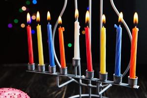 Jewish holiday Hanukkah background. A traditional dish is sweet donuts. Hanukkah table setting candlestick with candles and spinning tops on black background. Lighting Chanukah candles. Copy space photo