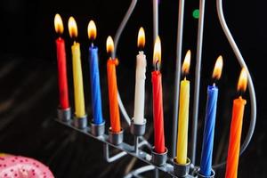 Jewish holiday Hanukkah background. A traditional dish is sweet donuts. Hanukkah table setting candlestick with candles and spinning tops on black background. Lighting Chanukah candles. Copy space photo