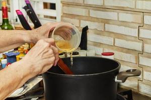 el chef vierte líquido en la olla de la cocina con estufa de gas