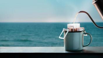 Dripping Coffee by the Sea Side at Morning. Making Hot Drink by Pouring Hot Water from kettle into an Instant Coffee Drip Bag at the Balcony. Relaxing with Harmony Living Lifestyle photo