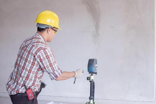 Worker in  measuring wall with laser leveler at construction site, Engineers at work checking construction building project with laser level machine during measurement work on site photo