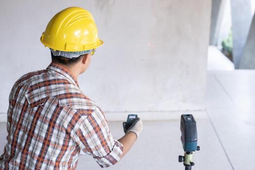 Worker in  measuring wall with laser leveler at construction site, Engineers at work checking construction building project with laser level machine during measurement work on site photo