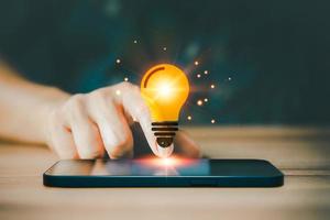 Glowing light bulb icon over a mobile phone or smartphone. Business idea, earning money, knowledge, learning, leadership, innovation and creativity concept photo