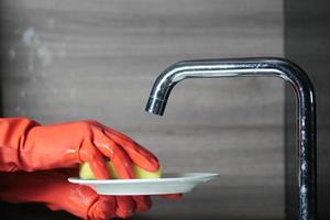 esponja, mano con guantes de goma rojos limpiando un plato con esponja foto