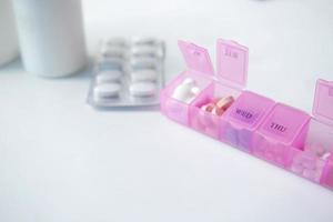 píldoras médicas en una caja de pastillas de color rosa sobre fondo blanco foto