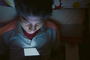 teenage boy sitting on sofa using smart phone at night photo