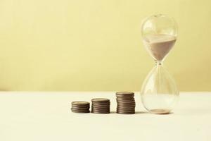 hourglass and stack of coins on table, photo