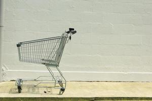 empty shopping trolley left outside against white wall photo