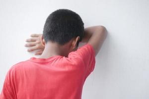 teenage boy head down against white wall photo