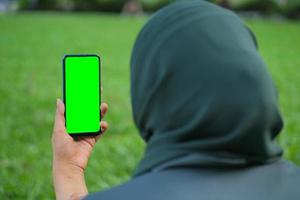 vista trasera de mujeres jóvenes usando un teléfono inteligente con pantalla verde sentada en el parque foto