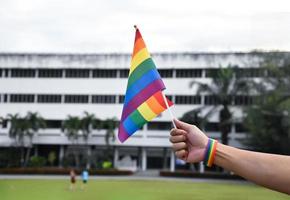 bandera del arco iris en la mano de un gay asiático que usa una pulsera arco iris para llamar y mostrar la diversidad de género lgbt y respetar la alternativa de género en todo el mundo. foto
