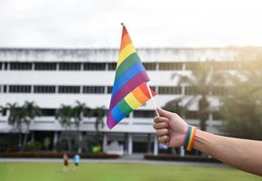 Rainbow flag holing in hand of asian gay which wears rainbow wristband to call out and shows LGBT gender diversity and respecting gender alternative around the world. photo