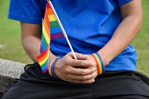 Rainbow flag holing in hand of asian gay which wears rainbow wristband to call out and shows LGBT gender diversity and respecting gender alternative around the world. photo