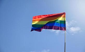 LGBT rainbow flag waving and holding in hands against blue sky in afternoon of the day, soft and selective focus, concept for lgbtqai celebration in pride month around the world. photo