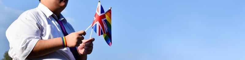 Union Jack flag and rainbow flag raising in hands and against bluesky, soft and selective focus, concept for LGBT celebrations and LGBT events in pride month in UK. photo