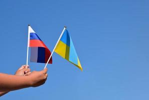 bandera nacional rusa y bandera nacional ucraniana cogidas de la mano contra el fondo azul, enfoque suave y selectivo. foto