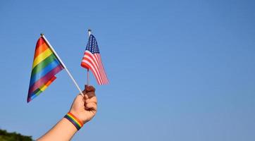 American flag and rainbow flag raising in hands and against bluesky, soft and selective focus, concept for LGBT celebrations and LGBT events in pride month in USA. photo