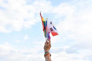 Rainbow flags and flags of many countries holding in hand against bluesky, concept for celebration of lgbtqai genders in pride month around the world, soft and selective focus. photo