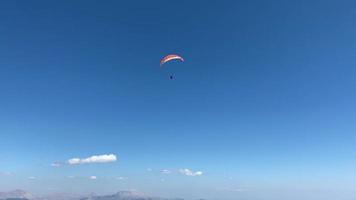 Ein Fallschirmspringer fliegt hoch in den blauen Himmel über wunderschöne Berge. Fallschirmspringen und Tourismus. qualitativ hochwertige Videos. 4k video