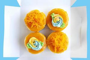 Top view of Cupcakes vintage Thai style and Gold egg yolk thread cakes in a open white paper box isolated on blue background. photo