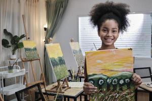 One Black student girl shows her painting work, proud with portfolio, acrylic color picture on canvas in art classroom and creative learning with talents skill at elementary school studio education. photo