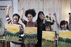 Group of art people in classroom studio, a teacher and student kids proud show painting work, an acrylic color picture on canvas, creative learning with talents skill at elementary school education. photo