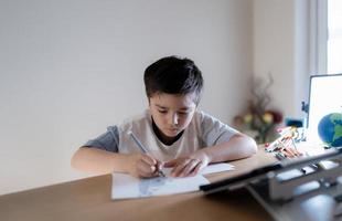 niño de la escuela que usa dibujos de pluma de color gris o esboza en papel, niño de retrato sentado en la mesa haciendo la tarea en la sala de estar, niño disfruta del arte y la actividad artesanal en casa el fin de semana, concepto de educación foto