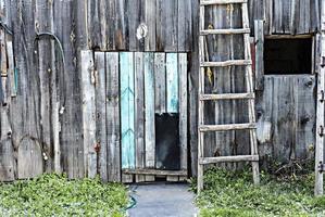 Old rustic gray blue wooden plank wall with dog walkway door and wooden staircase, white horseshoe above the entrance photo