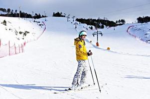 mujer joven sonriente feliz con chaqueta amarilla y casco de esquí esquiando en una ladera de montaña, deportes de invierno, actividad de esquí alpino al aire libre, estilo de vida saludable foto