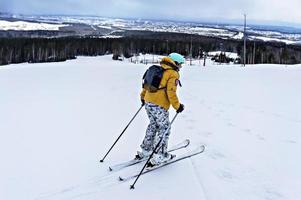 Young woman in yellow jacket and ski helmet skiing on a mountain slope, winter sports, alpine skiing outdoors activity, healthy lifestyle photo