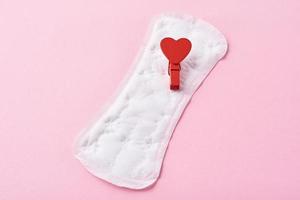 Sanitary pad and red wooden heart on a pink background photo