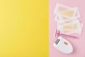 depiladora, maquinilla de afeitar y tiras de cera en amarillo y rosa foto